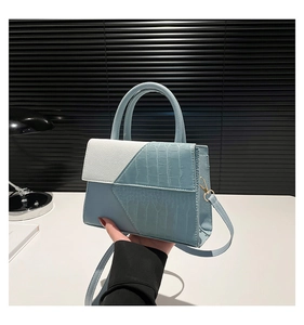 Détail du sac à main bleu et blanc texture crocodile avec finitions dorées et poignée chic