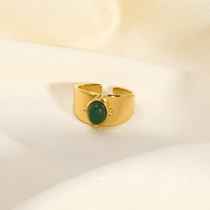 Macro shot of gold wide-band ring featuring a green oval stone on silk fabric