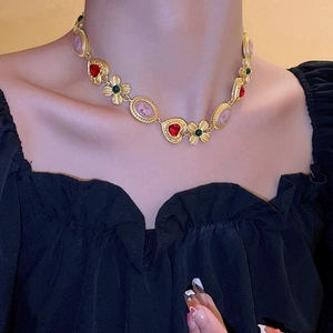 Close-up of vintage necklace with heart gem, flower, and pink cameo on a golden chain