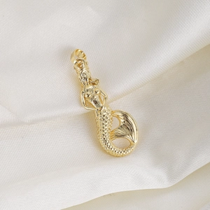 Detailed close-up of a golden mermaid pendant with intricate scales on white silk