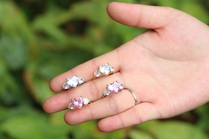 Close-up of four adjustable heart rings with pink and clear gems on a hand with leaf background