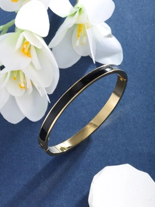 Detail view of gold and black stainless steel bangle with polished finish on blue background