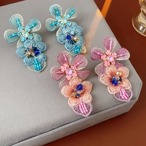 Macro detail of embroidered floral brooches with sequins on a grey velvet tray