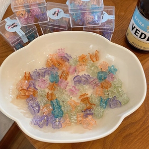 Close-up of colorful mini hair claw clips in a white bowl and transparent box packaging