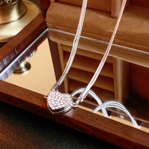 Detail of silver heart necklace with zircon inlay on snake chain over mirror reflection