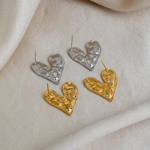 Détail de boucles d'oreilles cœur de lave plaquées or 18 carats et argent sur tissu beige