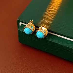Détail de créoles vintage dorées avec perles turquoise sur une boîte verte