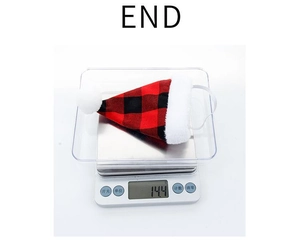Detail view of red and black plaid pet Christmas hat weighing 14.4g on digital scale