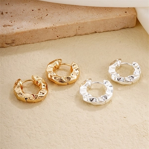 Minimalist textured gold and silver irregular hoop earrings displayed on stone props