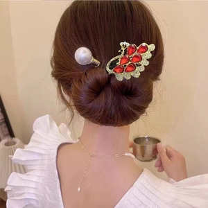 Détail d'une pince à cheveux paon dorée élégante avec cristaux rouges et perles