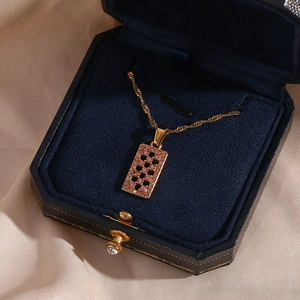 Macro view of gold rectangle maze pendant with pink gemstone in blue velvet box