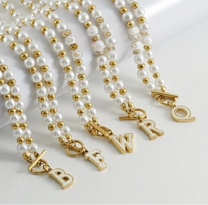 Détail de pendentifs lettres dorés 18K sur colliers de perles élégants