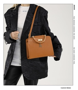 Detail of dark brown croc-embossed leather bag with golden ring handle and deer charm
