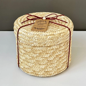 Detail of round straw gift box with woven texture, red string and thank you tag