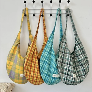 Row of four colorful plaid canvas tote bags in yellow, red, blue, and green hanging on wall