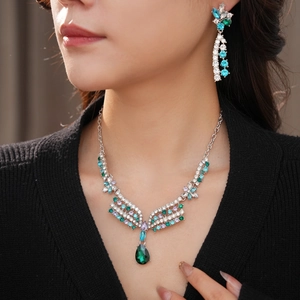 Close-up of elegant silver necklace and earring set with teal crystal teardrops on a model