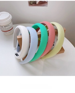 Detail showing five macaron-colored thick sponge headbands on a wooden display stand