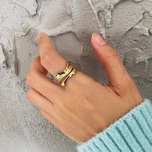 Close-up of an irregular wavy gold ring worn on a finger against a grey wall