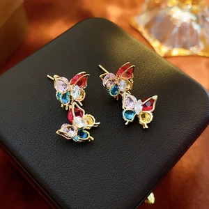 Macro shot of silver butterfly earrings with colorful zircon stones on a black jewelry box