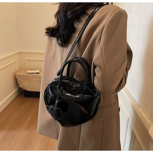 Détail du sac à main noir en forme de cœur avec un nœud chic et un pendentif assorti