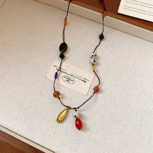 Dettaglio della collana boho con perline, pendente a goccia rosso e fiori di metallo