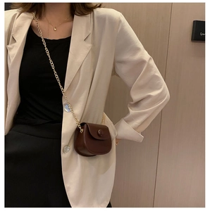 Détail d'un mini sac selle marron avec chaîne dorée porté par un mannequin mode