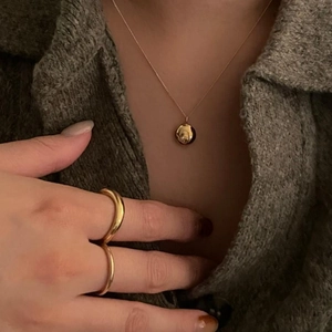Close-up of a textured gold round pendant necklace and matching rings on a grey sweater