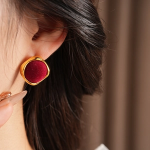 Gros plan d'une boucle d'oreille ronde en or avec velours rouge foncé sur un mannequin