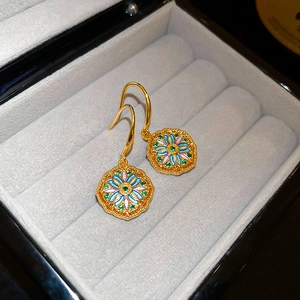 Detail of gold-plated floral earrings with colorful enamel and green central stone