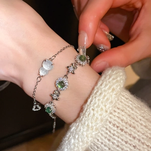 Close-up of stacked silver bracelets with white cat-eye stone and green floral zircon detail