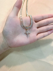 Detailed close-up of a gold cross necklace with sparkling zircons held in a hand