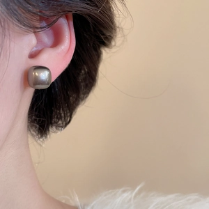 Macro shot of a minimalist square metal stud earring with a dark gunmetal mirror finish