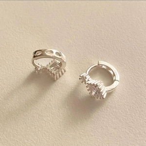 Macro shot of silver hoop earrings with clear square cubic zirconia on beige background