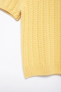 Dettaglio del top giallo a maniche corte in maglia a trecce con bordo inferiore a coste