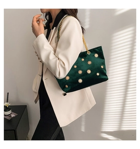 Detail of dark green velvet tote bag with gold floral ornaments and metal chain strap