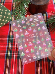 Detail of Christmas nail art stickers with gold foil trees and snowflakes held against decor