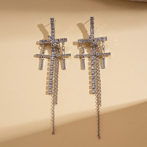 Close-up of silver cross tassel earrings with sparkling rhinestones and gothic details