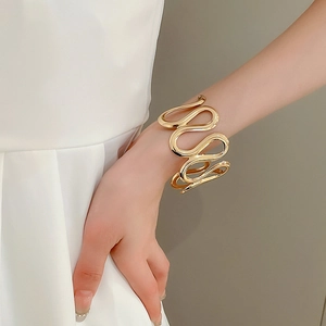 Detail of a gold wavy layered cuff bracelet showing metallic luster on a female wrist