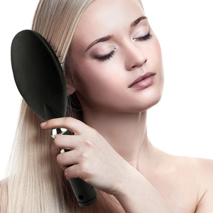 Close-up of a black air cushion hairbrush being used on long blonde hair