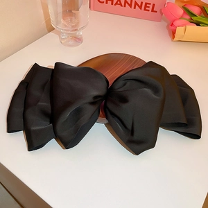 Gros plan sur une grande pince à cheveux en satin noir avec nœud sur plateau bois