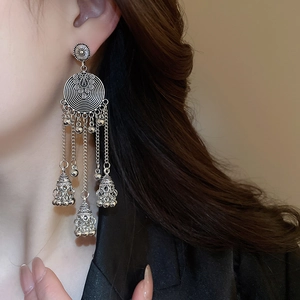 Macro detail of ethnic silver hoop earrings with chain tassels and bells on model