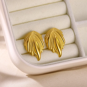 Macro detail of 18K gold wing earrings featuring brushed texture on silk background