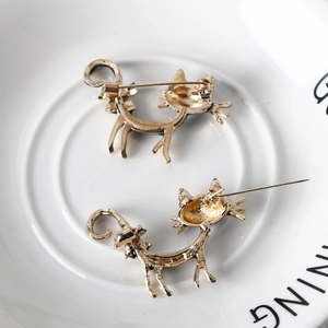 Golden metal cat brooches showing back pin structure and clasp details on white tray