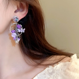 Vue détaillée de boucles d'oreilles fleur et papillon mauves avec strass sur modèle