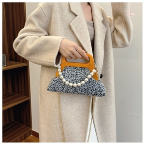 Close-up of black and white tweed handbag with wooden handle and elegant pearl chain trim