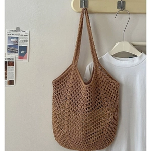 Brown hand-woven cotton tote bag with hollow mesh design hanging on wall for beach holidays