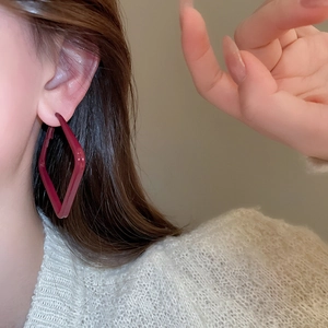 Detail of dark red geometric diamond earrings worn by a model in warm lighting