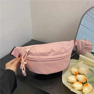 Close-up of pink crescent fanny pack with woven rope zipper pull on a dark desk
