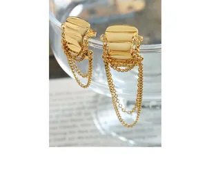 Macro view of gold chain tassels and wavy textured metal earrings on a glass rim