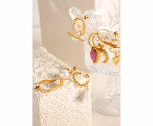 Artistic close-up of gold heart pendants, pearls and twisted metal earrings on stone